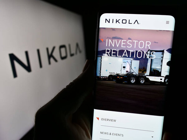 Stuttgart, Germany - 11-17-2023: Person holding cellphone with webpage of US electric vehicle company Nikola Corporation in front of logo. Focus on center of phone display.