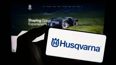 Stuttgart, Almanya - 11-22-2023: İsveçli elektrik ürünleri şirketi Husqvarna AB 'nin logosuna sahip akıllı telefon sahibi kişi web sitesinin önünde. Telefon ekranına odaklan.