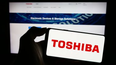 Stuttgart, Almanya - 11-23-2023: Japon elektronik şirketi Toshiba Corporation 'ın logosuyla cep telefonu tutan kişi iş sayfasının önünde. Telefon ekranına odaklan.
