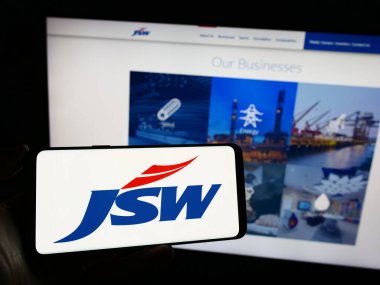 Stuttgart, Almanya - 11-23-2023: İş sayfasının önünde Hint holdingi JSW Group 'un logosunun bulunduğu cep telefonu sahibi kişi. Telefon ekranına odaklan.