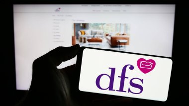 Stuttgart, Germany - 11-24-2023: Person holding cellphone with logo of British retail company DFS Furniture plc in front of business webpage. Focus on phone display. clipart