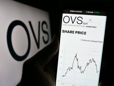 Stuttgart, Almanya - 11-24-2023: İtalyan moda şirketi OVS S.P.A. 'nın internet sayfası ile iş logosu önünde cep telefonu tutan kişi. Telefon ekranının merkezine odaklan.