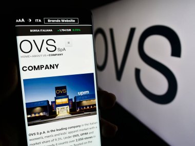 Stuttgart, Almanya - 11-24-2023: İtalyan moda şirketi OVS S.P.A. 'nın internet sayfası ile akıllı telefon taşıyan kişi iş logosu önünde. Telefon ekranının merkezine odaklan.