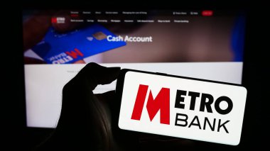 Stuttgart, Almanya - 11-24-2023: İngiliz finans hizmetleri şirketi Metro Bank plc 'nin logosunun bulunduğu cep telefonu sahibi kişi iş sayfasının önünde. Telefon ekranına odaklan.