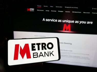 Stuttgart, Almanya - 11-24-2023: İngiliz finans hizmetleri şirketi Metro Bank plc 'nin logosuna sahip akıllı telefon sahibi kişi web sitesinin önünde. Telefon ekranına odaklan.