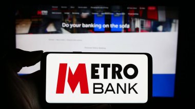Stuttgart, Almanya - 11-24-2023: İngiliz finans hizmetleri şirketi Metro Bank plc 'nin logosuyla cep telefonu sahibi kişi iş sayfası önünde. Telefon ekranına odaklan.