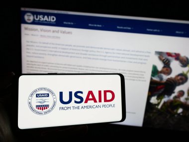 Stuttgart, Almanya - 11-27-2023: İnternet sayfası önünde ABD Uluslararası Kalkınma Dairesi (USAID) logosu olan cep telefonu sahibi kişi. Telefon ekranına odaklan.