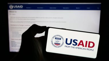 Stuttgart, Almanya - 11-27-2023: İnternet sayfası önünde ABD Uluslararası Kalkınma Dairesi (USAID) logosu bulunan kişi. Telefon ekranına odaklan.