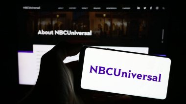 Stuttgart, Almanya - 11-27-2023: ABD 'li eğlence şirketi NBCUniversal Media LLLC' nin logosuna sahip cep telefonu sahibi kişi iş sayfasının önünde. Telefon ekranına odaklan.