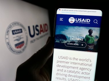 Stuttgart, Almanya - 11-27-2023: ABD Uluslararası Kalkınma Dairesi 'nin (USAID) logolu web sayfası ile cep telefonu tutan kişi. Telefon ekranının merkezine odaklan.