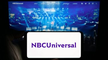 Stuttgart, Almanya - 11-27-2023: Amerikan eğlence şirketi NBCUniversal Media LLLC 'nin logosuyla cep telefonu tutan kişi iş sayfasının önünde. Telefon ekranına odaklan.