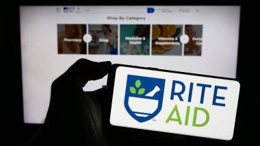 Stuttgart, Almanya - 11-27-2023: Üzerinde ABD 'li eczane şirketi Rite Aid Corporation' ın logosu bulunan cep telefonu sahibi kişi iş sayfası önünde. Telefon ekranına odaklan.
