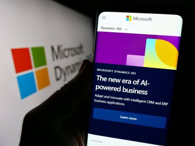 Stuttgart, Almanya - 11-27-2023: Muhasebe yazılım ürünü Microsoft Dynamics 365 sayfasıyla logo önünde akıllı telefon tutan kişi. Telefon ekranının merkezine odaklan.