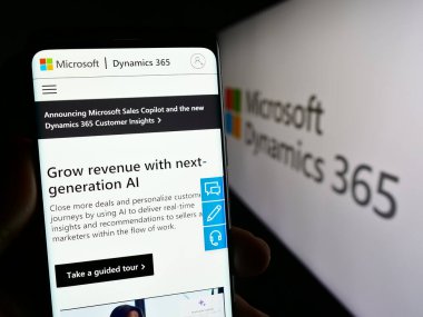 Stuttgart, Almanya - 11-27-2023: Muhasebe yazılım ürünü Microsoft Dynamics 365 sayfasıyla birlikte logo önünde cep telefonu tutan kişi. Telefon ekranının merkezine odaklan.