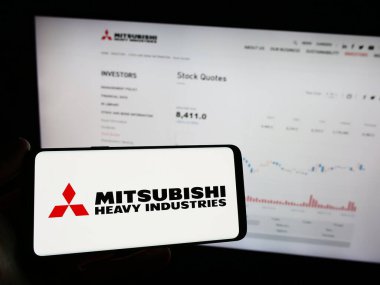 Stuttgart, Almanya - 11-28-2023: Japon Mitsubishi Heavy Industries Ltd. (MHI) şirketinin logosuna sahip cep telefonu sahibi kişi web sayfası önünde. Telefon ekranına odaklan.