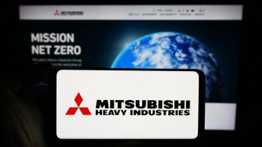 Stuttgart, Almanya - 11-28-2023: İnternet sitesi önünde üzerinde Mitsubishi Heavy Industries Ltd. (MHI) adlı Japon şirketinin logosu bulunan kişi. Telefon ekranına odaklan.