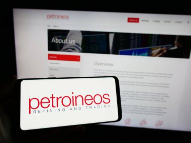 Stuttgart, Germany - 11-28-2023: Person holding smartphone with logo of British oil and gas company PetroIneos Trading Limited in front of website. Focus on phone display. clipart