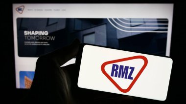 Stuttgart, Almanya - 11-28-2023: Hintli emlak yatırım şirketi RMZ Corp 'un logosuna sahip akıllı telefon sahibi kişi web sitesinin önünde. Telefon ekranına odaklan.