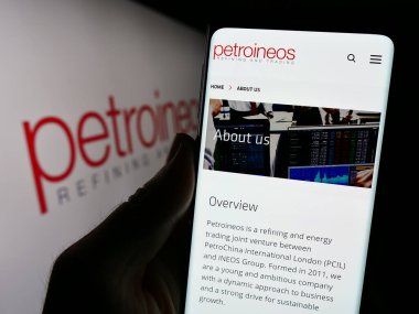 Stuttgart, Almanya - 11-28-2023: İngiliz petrol ve gaz şirketi PetroIneos Trading Limited 'in logolu web sayfası ile cep telefonu tutan kişi. Telefon ekranının merkezine odaklan.