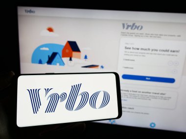 Stuttgart, Almanya - 11-29-2023: İnternet sayfasının önünde Amerikan tatil kiralama pazar yeri şirketi Vrbo 'nun logosuna sahip cep telefonu sahibi kişi. Telefon ekranına odaklan.