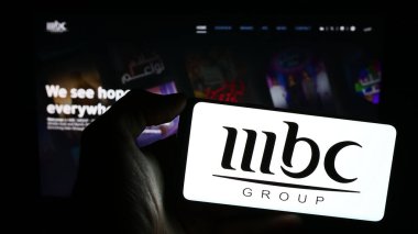 Stuttgart, Almanya - 11-29-2023: Suudi Arabistan medya şirketi MBC Group 'un logosuyla cep telefonu tutan kişi iş sayfası önünde. Telefon ekranına odaklan.