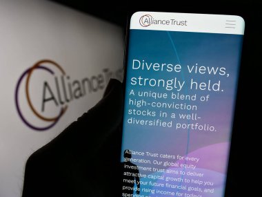 Stuttgart, Almanya - 11-30-2023: İngiliz yatırım şirketi Alliance Trust plc 'in web sayfası ile logo önünde cep telefonu tutan kişi. Telefon ekranının merkezine odaklan.