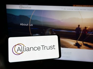 Stuttgart, Almanya - 11-30-2023: İngiliz yatırım şirketi Alliance Trust 'ın logosunun bulunduğu akıllı telefonu web sitesinin önünde tutan kişi. Telefon ekranına odaklan.