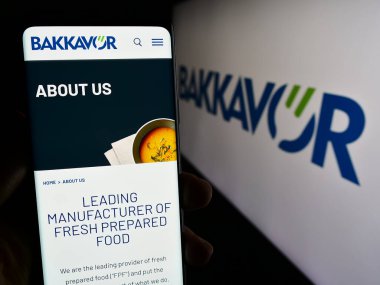 Stuttgart, Almanya - 12-02-2023: Logo önünde gıda işleme şirketi Bakkavor Group plc 'nin web sayfası ile akıllı telefon tutan kişi. Telefon ekranının merkezine odaklan.
