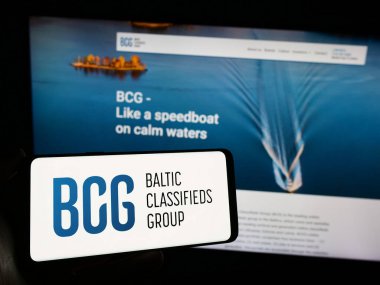 Stuttgart, Germany - 12-02-2023: Person holding smartphone with logo of Lithuanian company Baltic Classifieds Group plc (BCG) in front of website. Focus on phone display. clipart