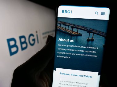 Stuttgart, Almanya - 12-02-2023: Yatırım şirketi BBGI Global Altyapı S.A. 'nın web sayfası ile logo önünde cep telefonu tutan kişi. Telefon ekranının merkezine odaklan.