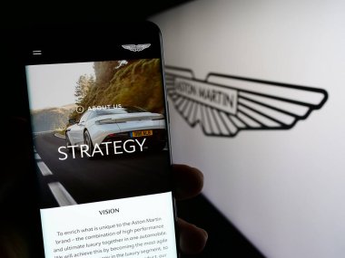 Stuttgart, Almanya - 12-02-2023: İngiliz Aston Martin Lagonda Global Holding 'in logolu web sayfası ile cep telefonu tutan kişi. Telefon ekranının merkezine odaklan.