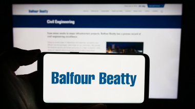 Stuttgart, Almanya - 12-02-2023: İngiliz altyapı şirketi Balfour Beatty plc 'nin logosuyla cep telefonu sahibi kişi iş sayfasının önünde. Telefon ekranına odaklan.