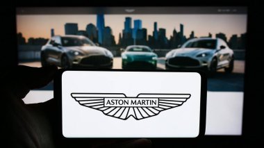 Stuttgart, Germany - 12-02-2023: Person holding cellphone with logo of British company Aston Martin Lagonda Global Holdings plc in front of webpage. Focus on phone display. clipart