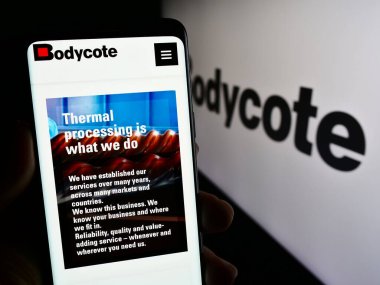 Stuttgart, Almanya - 12-05-2023: İngiliz mühendislik hizmetleri şirketi Bodycote plc 'nin web sayfası ile logo önünde cep telefonu tutan kişi. Telefon ekranının merkezine odaklan.