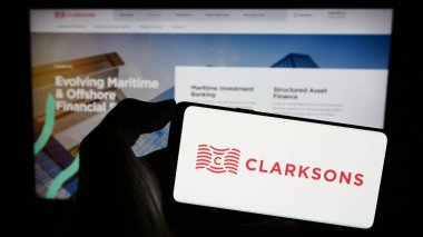Stuttgart, Almanya - 12-06-2023: İngiliz lojistik şirketi Clarkson plc 'ın (Clarksonlar) logosuna sahip akıllı telefon sahibi kişi. Telefon ekranına odaklan.