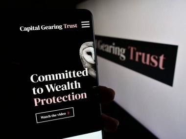 Stuttgart, Germany - 12-06-2023: Person holding cellphone with webpage of British investment company Capital Gearing Trust plc (CGT) with logo. Focus on center of phone display. clipart