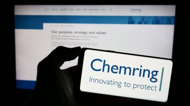 Stuttgart, Germany - 12-06-2023: Person holding smartphone with logo of British aerospace and defence company Chemring Group plc in front of website. Focus on phone display. clipart