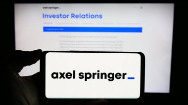 Stuttgart, Almanya - 12-07-2023: Alman kitle iletişim şirketi Axel Springer SE 'nin logosuyla cep telefonu tutan kişi iş sayfasının önünde. Telefon ekranına odaklan.