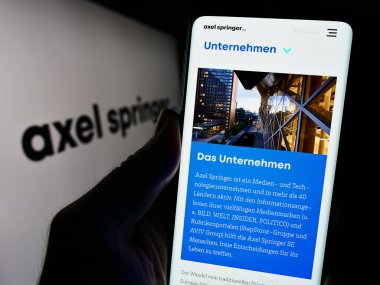 Stuttgart, Almanya - 12-07-2023: Alman kitle iletişim kuruluşu Axel Springer SE 'nin internet sayfası ile iş logosu önünde cep telefonu tutan kişi. Telefon ekranının merkezine odaklan.