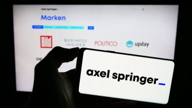 Stuttgart, Almanya - 12-07-2023: Alman kitle iletişim şirketi Axel Springer SE 'nin logosunu taşıyan cep telefonu sahibi kişi iş sayfasının önünde. Telefon ekranına odaklan.