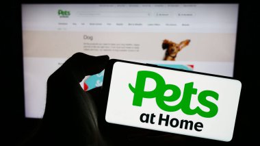 Stuttgart, Almanya - 12-07-2023: İngiliz malzeme perakende şirketi Pets in Home Group 'un logosuna sahip cep telefonu sahibi kişi iş sayfası önünde Home Group' ta. Telefon ekranına odaklan.