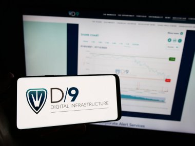 Stuttgart, Almanya - 12-08-2023: İngiliz Digital 9 Altyapı plc (D9) şirketinin logosuna sahip cep telefonu sahibi kişi iş sayfasının önünde. Telefon ekranına odaklan.