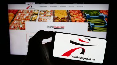 Stuttgart, Almanya - 12-08-2023: İnternet sayfası önünde Fransız ITM Entreprises SA (Les Mousquetaires) logosu olan cep telefonu sahibi kişi. Telefon ekranına odaklan.