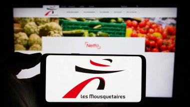 Stuttgart, Almanya - 12-08-2023: İnternet sayfası önünde üzerinde Fransız ITM Entreprises S.A. (Les Mousquetaires) logosu bulunan kişi. Telefon ekranına odaklan.