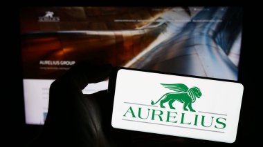 Stuttgart, Almanya - 12-08-2023: Avrupalı yatırım şirketi Aurelius Group 'un logosuna sahip cep telefonu sahibi kişi iş sayfasının önünde. Telefon ekranına odaklan.
