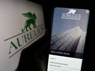 Stuttgart, Almanya - 12-08-2023: Avrupalı yatırım şirketi Aurelius Group 'un web sayfası ile logo önünde akıllı telefon tutan kişi. Telefon ekranının merkezine odaklan.