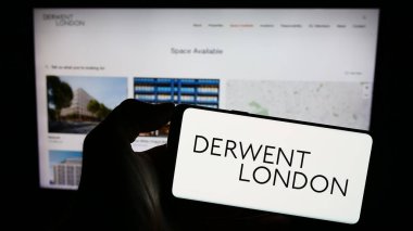 Stuttgart, Germany - 12-08-2023: Person holding smartphone with logo of British real estate company Derwent London plc in front of website. Focus on phone display. clipart