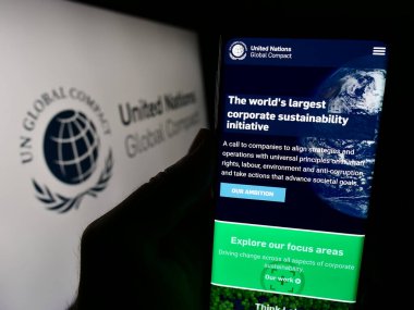 Stuttgart, Almanya - 12-09-2023: BM Paktı Birleşmiş Milletler Global Compact web sayfası ile logo önünde cep telefonu tutan kişi. Telefon ekranının merkezine odaklan.
