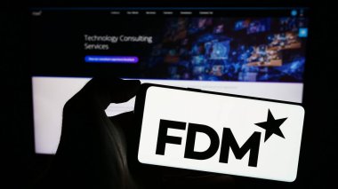 Stuttgart, Almanya - 12-09-2023: İngiliz bilgi teknolojileri şirketi FDM Group Limited 'in logosuna sahip akıllı telefon sahibi kişi web sitesi önünde. Telefon ekranına odaklan.