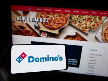Stuttgart, Almanya - 12-09-2023: İnternet sitesinin önünde ABD 'li restoran zinciri Domino' s Pizza Inc. 'in logosuna sahip kişi. Telefon ekranına odaklan.